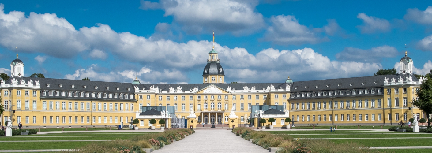 Blick auf das Karlsruher Schloss mit seiner gelben Fassade und den vielen Fenstern. Der Himmel ist blau.