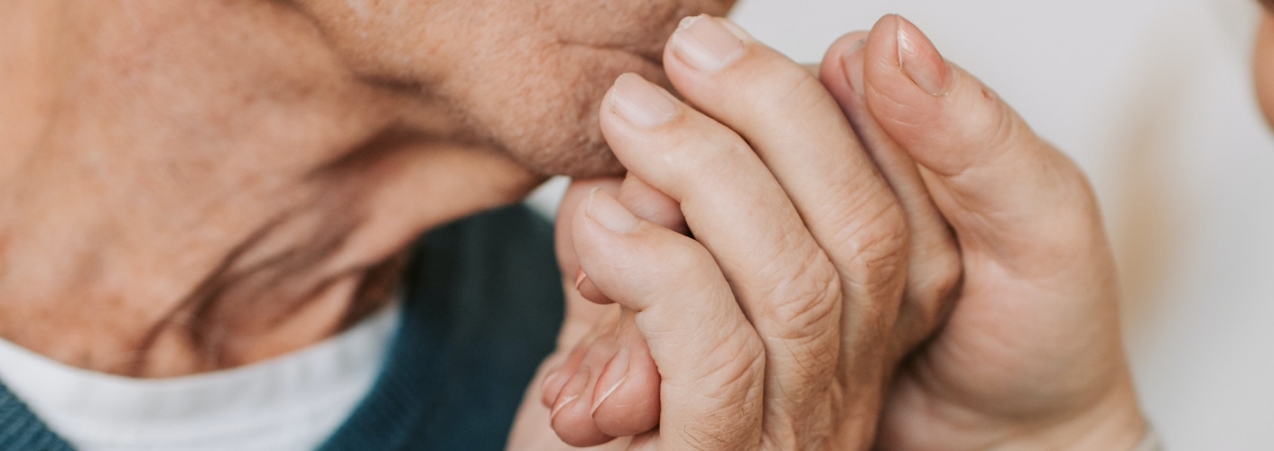Ein Mann hält die Hand einer Frau und küsst diese. Das symbolisiert Hilfe und Unterstützung.